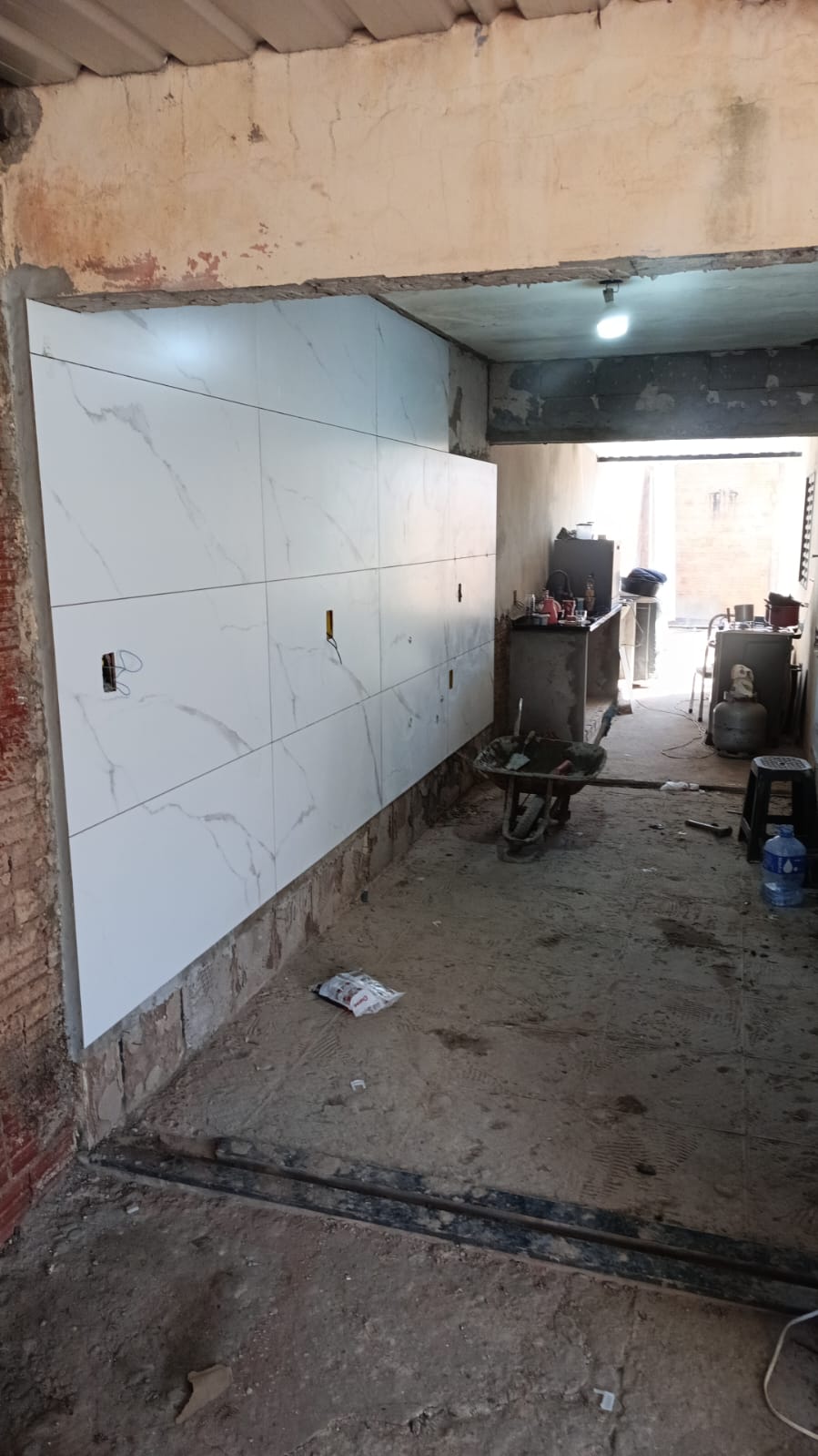parede recém revestida com porcelanato branco marmoreado em obra de cozinha, com carrinho de mão e botijão de 